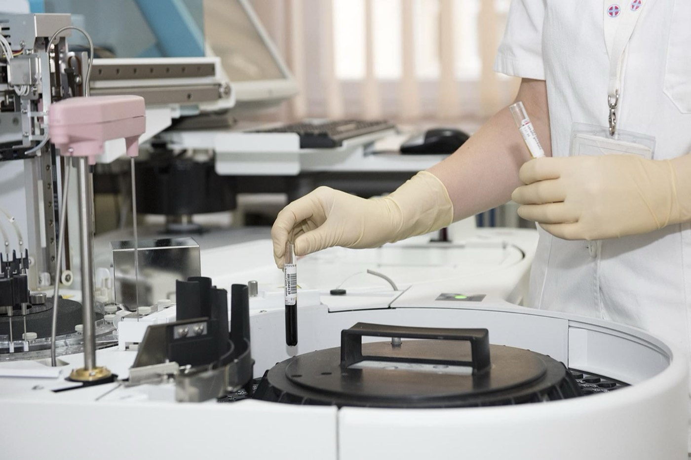 Profissional de luvas posicionando um tubo de sangue em uma centrífuga de laboratório